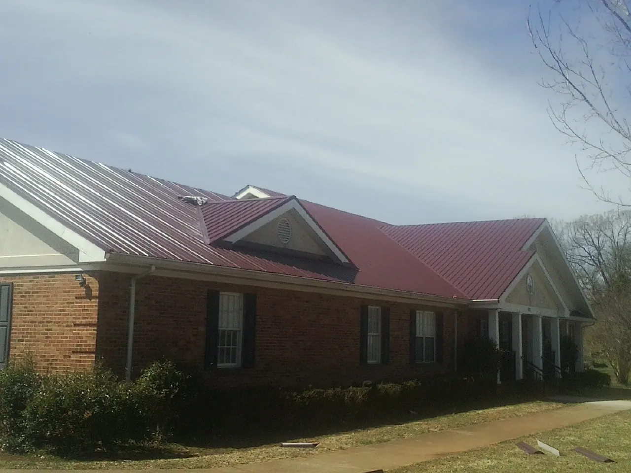 Red metal roof with gabled entries on a long brick building, from a Hail Damage Roof Repair job in Belmont